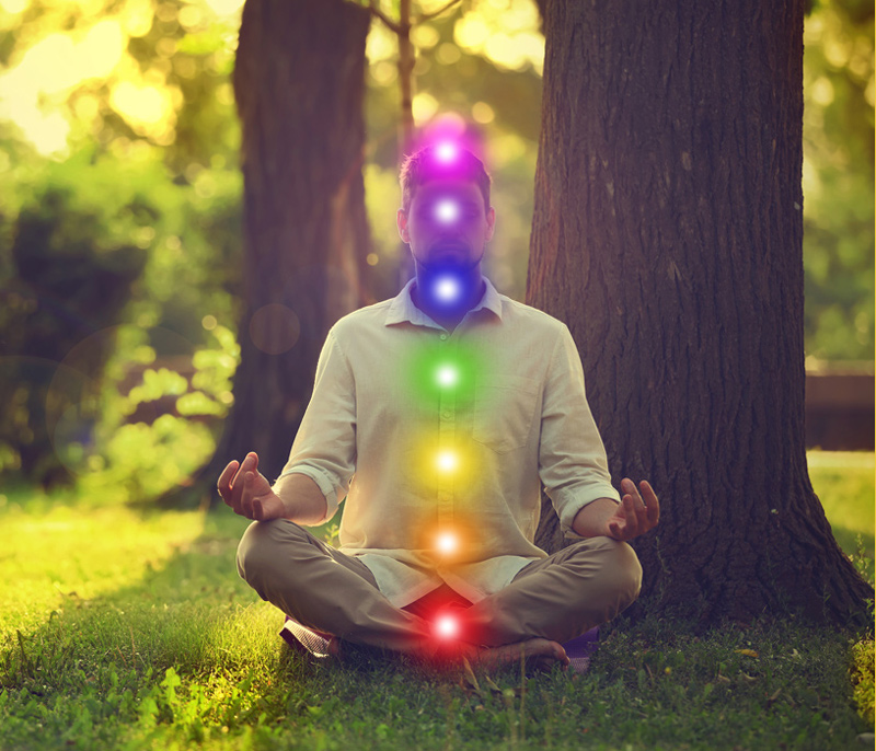 A man meditating in the woods with the 7 chakra colors laid over his body.