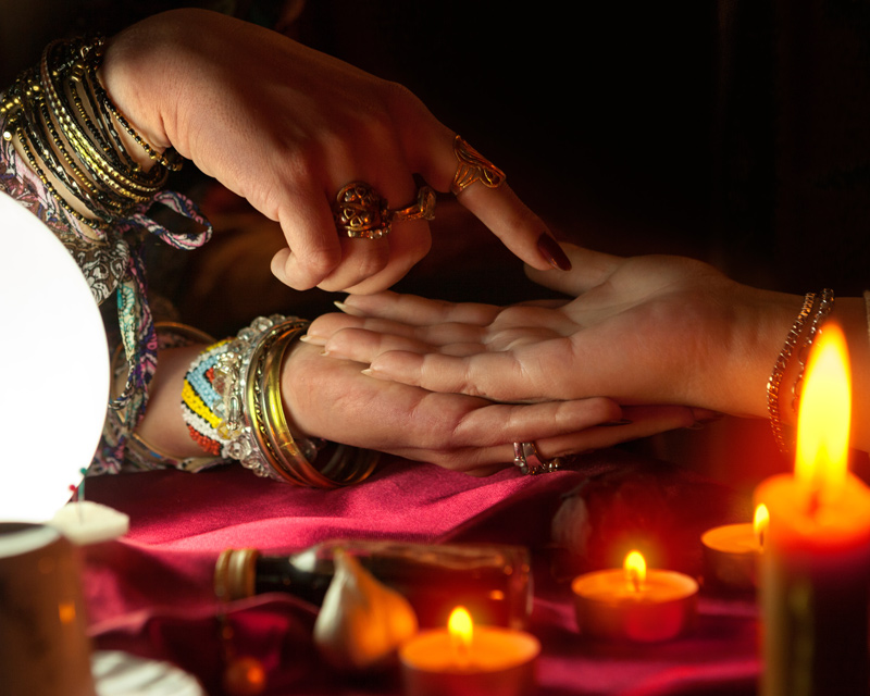 A psychics hand is pointing to the lines on a woman's hand during a palm reading.
