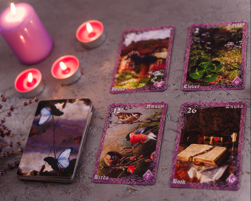 Purple-edged tarot cards laid out on a table next to some burning candles.
